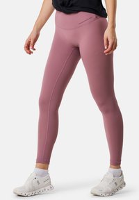 Rosa sports leggings med høj talje, glat tekstur og vertikal syning, båret med hvide sneakers og ankelstrømper.