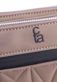 Cartera de tela beige con detalle texturizado y sección de cremallera azul oscuro. Herrajes de plata con el logo "cta" grabado en la superficie.