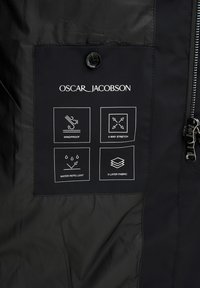 Schwarzer Windbreaker-Stoff mit einem Etikett, das weiße Symbole für winddicht, 4-Wege-Stretch, wasserabweisend und 3-lagiges Material zeigt.