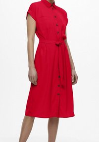 Robe rouge à manches courtes avec col, boutonnage sur le devant et ceinture à la taille. Dispose de deux poches poitrine et d’une coupe décontractée.