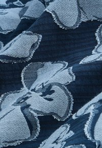 Tamsiai mėlynas audinys su didelėmis šviesiai mėlynomis gėlėmis, kuriame matyti nuskelti kraštai ir tekstūruoti austų detalių raštai.