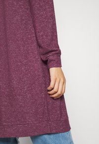 Långärmad, vinröd topp i texturerad tyg, med en lös passform och en rundad nederkant, parat med ljusblå denim.