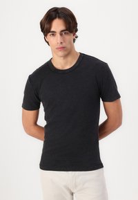 Sort t-shirt med korte ærmer og rund hals, der har en blød, glat tekstur og en tætsiddende design. Båret med lysfarvede bukser.