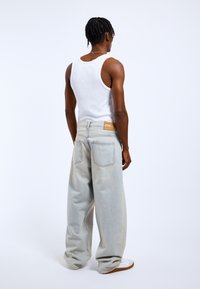 Jasnoniebieskie dżinsy o luźnym kroju, z wysokim stanem, dwiema tylnymi kieszeniami i beżową metką marki na pasku.