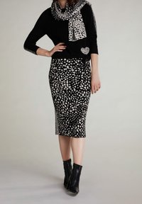 Musta neule, jossa on sydänkoristelu, kuvioitu hame musta- ja kermaapohjaisena, yhdistettynä vetoketjullisiin mustiin nilkkureihin. Huivissa on samanlainen kuvio.