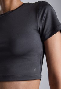 Black fitted t-shirt with short sleeves, smooth texture, subtle seam detailing, and a small logo at the hem.