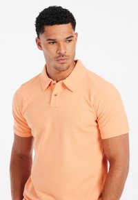 Oranje poloshirt van gestructureerde stof, met een klassieke kraag en een knoopsluiting met drie knopen, korte mouwen en een fitted model.