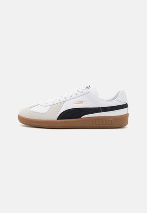 Sneaker blanc avec bande noire Puma, semelle en gomme, sur-couche en daim beige, et logo Puma doré sur le côté, présenté sur fond blanc.
