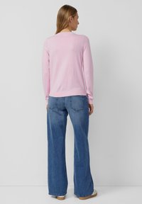 Jasnoróżowy sweter z długimi rękawami, z okrągłym dekoltem. Do tego szerokie, niebieskie dżinsy o luźnym kroju i casualowym stylu.