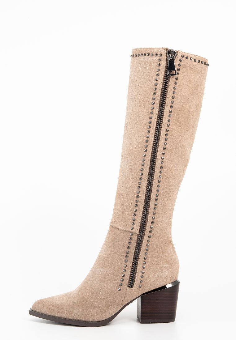 Bota de ante beis hasta la rodilla con dos cremalleras y acentos de tachuelas en las costuras, con un tacón bloque para mayor soporte.