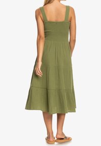 Vestido midi verde en capas con tirantes anchos, cuerpo fruncido y una falda fluida. La tela tiene un acabado texturizado y suave.