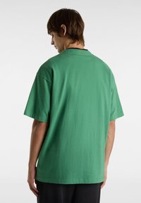 T-shirt en coton vert avec une coupe décontractée, des manches courtes et un col rond, présentant une texture unie et un minimum de détails au dos.
