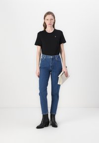 Crna majica, traperice s visokim strukom u plavoj boji i crne gležnjače. Model drži bež clutch torbicu sa zatvaranjem na patentni zatvarač. Jednostavan, krojen dizajn.