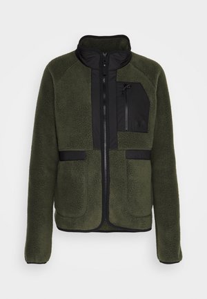 Chaqueta de forro polar en verde oscuro con un frente con cremallera negra y un bolsillo en el pecho. Presenta un cuello alzado y un diseño de paneles en contraste.