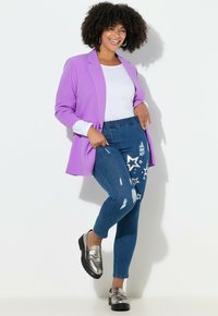 Fioletowa marynarka na białym topie, do tego niebieskie dżinsy z nadrukiem gwiazd i przetarciami, uzupełnione metalicznymi butami.