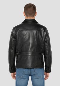 Veste de moto en cuir noir avec un col, des coutures détaillées, des sangles latérales réglables à boucle, et des poignets boutonnés, portée sur un jean bleu.