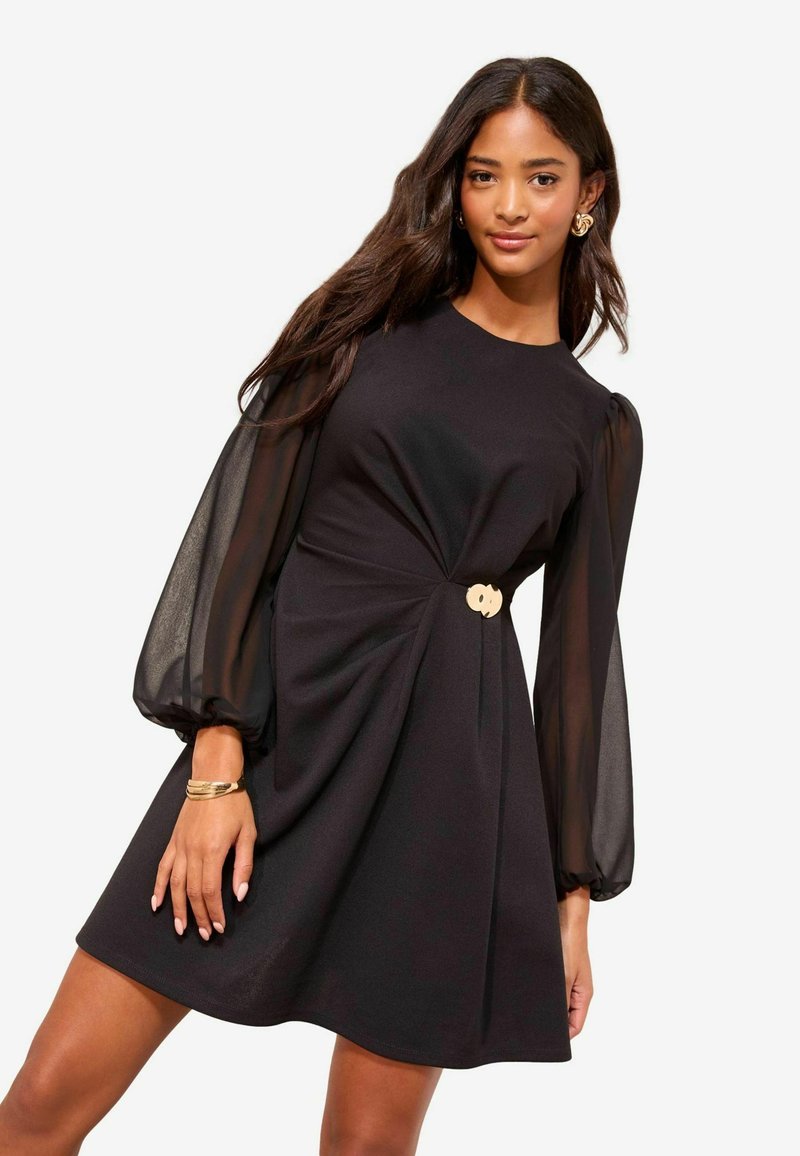 Schwarzes Kleid mit tailliertem Oberteil und ausgestelltem Rock, ausgestattet mit transparenten Puffärmeln und einem goldenen Akzent in der Taille. Durchgehend glatte Textur.