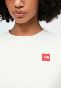 Ανοιχτό γκρι φούτερ με στρογγυλή λαιμόκοψη, που διαθέτει κόκκινο κομμένο λογότυπο στο αριστερό στήθος. Μαλακή υφή από βαμβάκι.