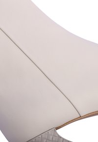 Zapato de cuero blanco con una superficie lisa y un diseño redondeado, que presenta una suela gris texturizada y un detalle de costura sutil a lo largo de la parte superior.