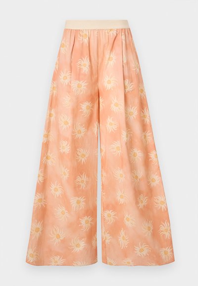 Wide-legged trousers in light peach fabric featuring a sun pattern in white with yellow centers, an elastic waistband, and a soft texture.
