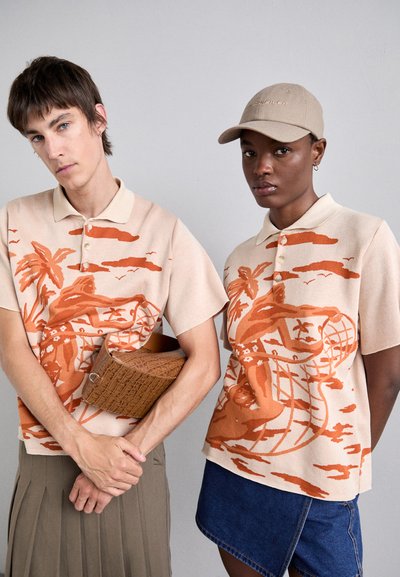 Beige polo shirts hebben oranje grafische patronen van palmbomen en figuren, gecombineerd met een gestructureerde bruine tas en een beige pet.