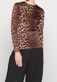 Leopardmönstrad långärmad skjorta i nyanser av brunt och svart, tillverkad av ett mjukt, stretchy material, i kombination med lösa svarta byxor.