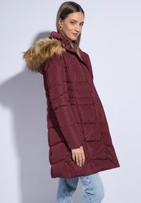 Burgundská puffrová bunda s umělou kožešinou na kapuci, prošívaný design a dlouhé rukávy. Obsahuje patentní knoflíky a boční kapsy.
