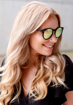 Black sunglasses with green reflective lenses, featuring a round shape and the brand name "VUCH" printed on the frame. Long, wavy blonde hair.