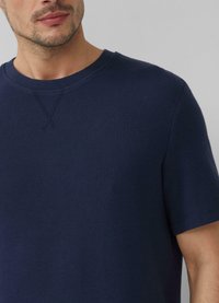 Marineblauwe t-shirt met korte mouwen, gemaakt van gestructureerde stof. Beschikt over een ronde hals met subtiele kruissteekdetails bij de kraag.
