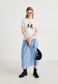 White cotton t-shirt featuring a graphic of Mickey and Minnie Mouse; light blue denim skirt with buttons; black ankle boots; black handbag.