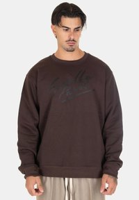 Felpa marrone realizzata in tessuto morbido, con colletto rotondo e maniche lunghe. Design con scritte nere sul davanti; vestibilità comoda.