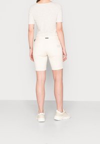 Wit gestreept topje met korte mouwen, gecombineerd met crèmegekleurde aangesloten shorts met zakken en een subtiel logodetail aan de achterkant.