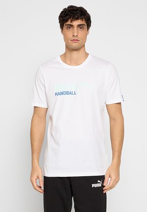 Mand med kort mørkt hår iført en hvid Puma håndbold t-shirt og sorte Puma bukser, stående mod en ensfarvet baggrund.