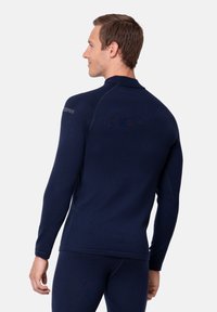 Granatowy, długorękawowy top termiczny o dopasowanym kroju, z wysokim kołnierzem i bezszwową konstrukcją ramion. Posiada subtelne logo na rękawie.