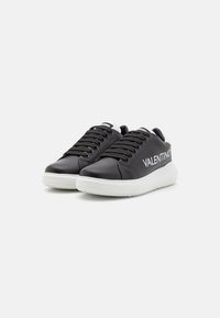 Mustad nahkkingad valge kummitaldiga, millel on lamedad mustad paelad ja küljel on valgele trükitud "VALENTINO".