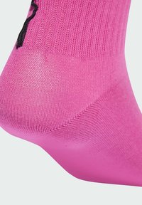 Calzino rosa con un design a maglia testurizzato e tallone rinforzato, con una suola liscia. Dettaglio del marchio nero visibile di lato.