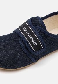 Mornarska slip-on cipela izrađena od teksturiranog materijala s čičak trakama i crno-bijelom oznakom. Fleksibilna gumena potplat.