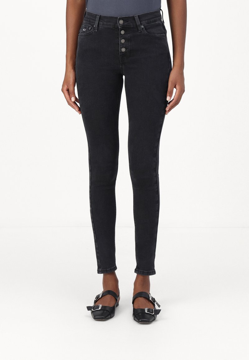 Fekete, magas derekú, skinny farmernadrág öt gombos elülső záródással, karcsú fazonnal és minimalista hátsó zsebekkel. Simaságával zárul.