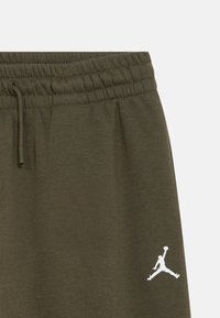 Ελαστικό παντελόνι φόρμας σε ελιά πράσινο με κορδόνι στη μέση και κεντημένο λευκό λογότυπο του παίκτη μπάσκετ Jumpman κοντά στην τσέπη.