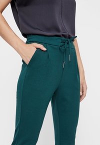 Gröna joggingbyxor i mjukt, texturerat material. Utrustade med resårmidja med snörning, sidofickor och en avsmalnande bendesign.