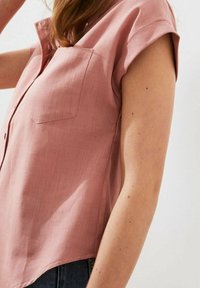 Chemise rose à manches courtes avec un col pointu, ouverture par boutons et poche sur la poitrine gauche, confectionnée en tissu léger et texturé.