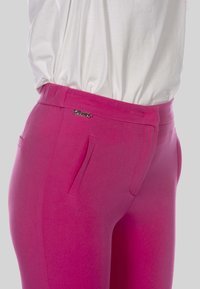Fuchsia roze nauwsluitende broek gemaakt van rekbaar materiaal met een gladde textuur, voorzien van zijzakken en een decoratieve metalen accent op de tailleband.