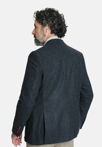 Blazer de un oscuro azul marino hecho de tela texturizada. Presenta solapas con muesca, una abertura simple y acentos de botones marrones en las muñecas.