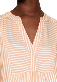 Blusa a rayas melocotón y crema con escote en V, mangas cortas y detalle fruncido en la cintura. Tejido ligero y texturizado.