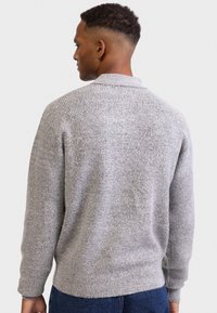 Grå strikket genser med et teksturert mønster, med krage og lange ermer, sett bakfra, sammen med blå jeans.