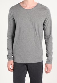 Gray long-sleeve t-shirt made of soft, lightweight material with a rounded neckline and fitted sleeves, paired with dark pants.