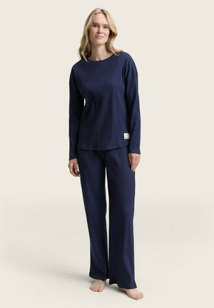 Navyblauw geribd pyjama set met een langemouwen top en losse broek. De stof heeft een zachte textuur; etiket zichtbaar op de zoom van de top.