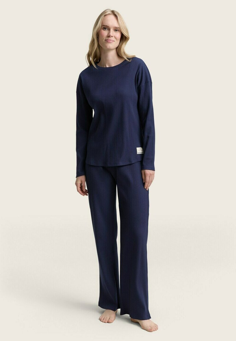 Navyblauw geribd pyjama set met een langemouwen top en losse broek. De stof heeft een zachte textuur; etiket zichtbaar op de zoom van de top.