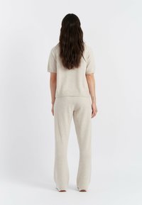 Completo in maglia beige con top a maniche corte e pantaloni a gamma ampia. Texture morbida, bordi a coste e design minimalista. Vista da dietro.