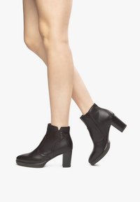 Black leather ankle boots with a block heel, side zipper, and a cut-out design at the collar. Smooth texture with minimal accents.